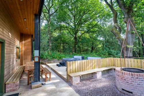 a patio with benches and a fence with trees at Throwley, woodland lodge with hot tubs for 14 in Oakamoor