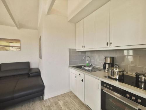 Una cocina con gabinetes blancos y un sofá negro en ella. en Wohnung 02, en Horumersiel