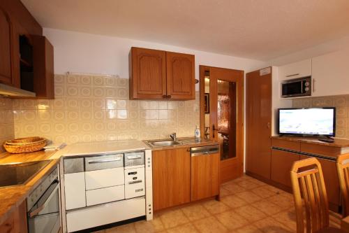 a kitchen with wooden cabinets and a tv on the wall at Ferienwohnung im Zentrum von Kappl Paznauntal PAZN100 by FeWo-PLAN in Kappl