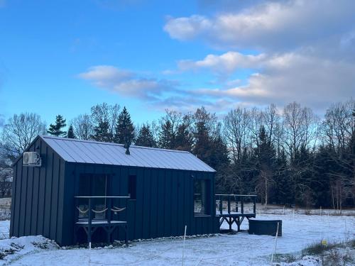 a black shed in a snowy field with trees at Holiday Hill Karpnki, Sauna, Domek Hygge-balia, Domek Lagom-jacuzzi in Karpniki