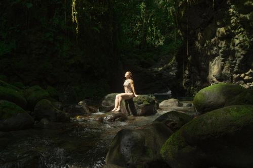 a woman sitting on a rock in a river at Ecolirios Boutique Hotel & Villas in Guácimo