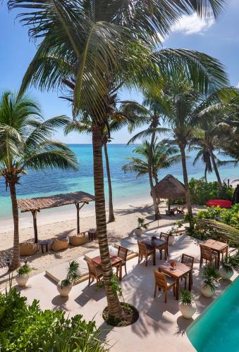 a beach with tables and palm trees and the ocean at Mantaray Tulum in Tulum