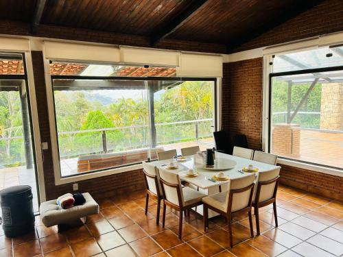 a dining room with a table and chairs and windows at Chacara pé na agua represa de Mairiporã in Mairiporã