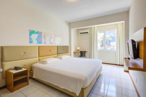 a bedroom with a large white bed and a television at GoldMen Business Joinville in Joinville