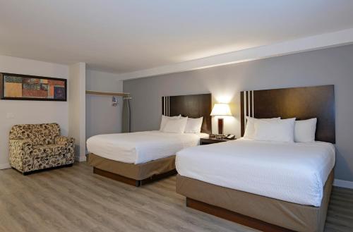 a hotel room with two beds and a chair at Travelodge by Wyndham Kamloops Mountview in Kamloops