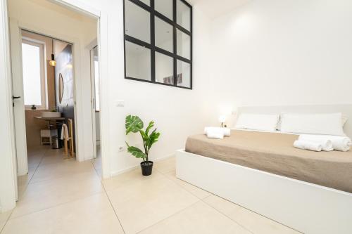 a white bedroom with a large bed and a plant at Valguarnera Studio Apartments in Palermo