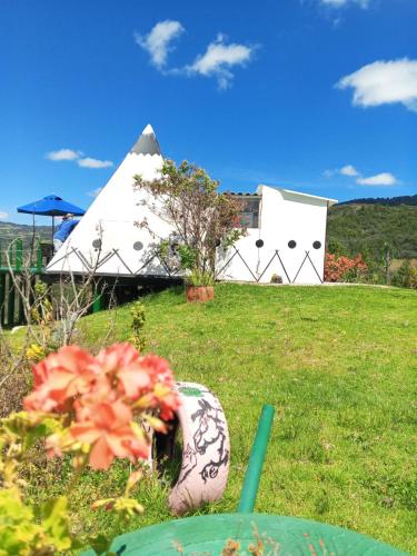 a white tent in the grass with flowers in a yard at Glamping Mafer 4 Tipi pequeño in Guatavita