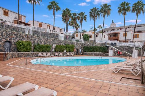a swimming pool with chairs and palm trees at Paradise Dúplex Garden & Beach Maspalomas in San Bartolomé