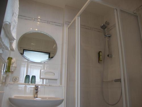 ein Bad mit einem Waschbecken und einer Dusche mit einem Spiegel in der Unterkunft Hotel Bergschlößchen in Pockau