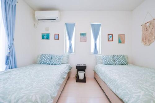two beds in a room with white walls and windows at Villa Fukugi in Motobu