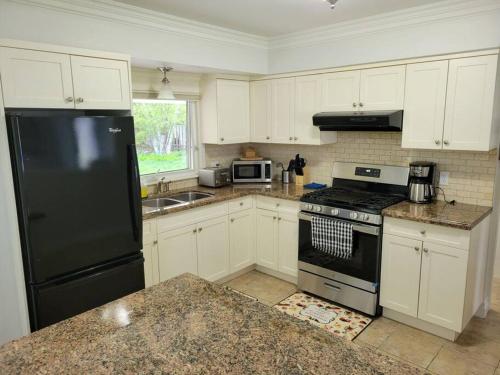 a kitchen with white cabinets and a black refrigerator at Cozy Urban Cottage Close to Lake Ontario in Burlington