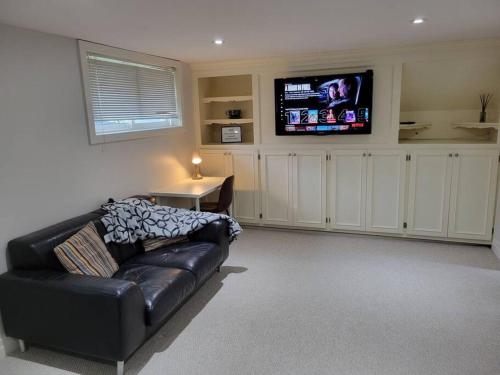 a living room with a black leather couch and a flat screen tv at Cozy Urban Cottage Close to Lake Ontario in Burlington