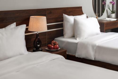 a hotel room with two beds and a table with a lamp at Astoria Hanoi Hotel & Travel in Hanoi