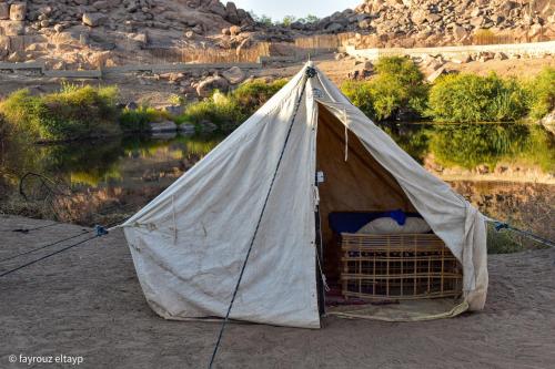 a tent sitting next to a body of water at ASSINGAR camp in Jazīrat Suhayl