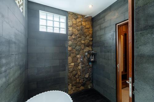 a bathroom with a shower with a stone wall at Puri Andong Villa in Ubud