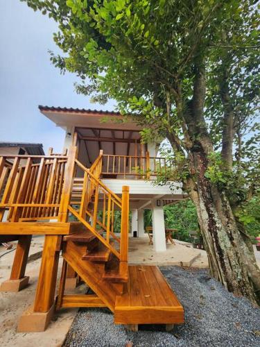 a house with a wooden staircase next to a tree at Rimtara Nan ริมธารา น่าน in Ban Khia