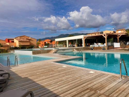 a swimming pool with a wooden deck and a building at Appartement CERICA proche de la plage de Saint Cyprien in Lecci