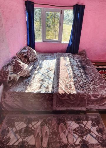 a bedroom with a bed with a window and shoes at Mudhouse Cottage in Apple Orchard - Sainj Valley in Sainj