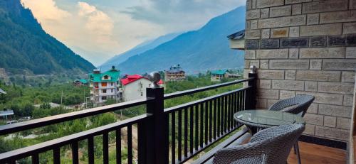 a balcony with chairs and a table and a view of mountains at Nazaara - A Luxe Retreat in Manāli