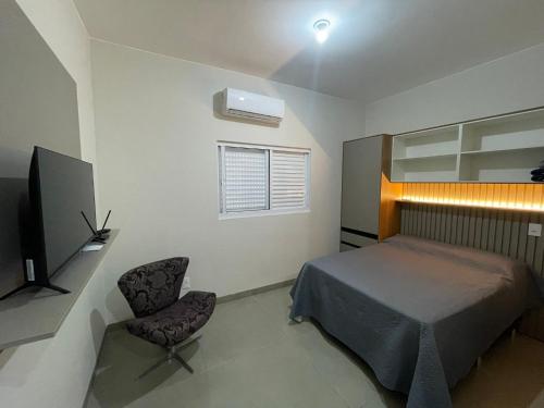 a bedroom with a bed and a tv and a chair at Studio 105 in Primavera do Leste