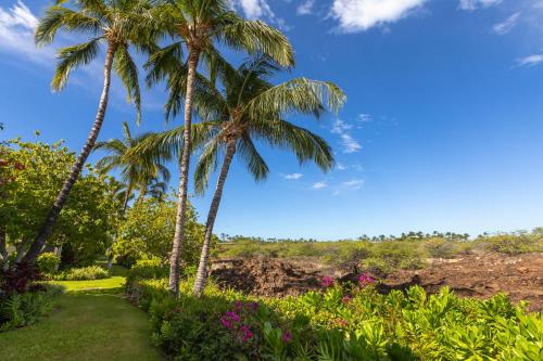 two palm trees in a garden with flowers at Mauna Lani Palm Villas D-2 Corner Unit Historic View in Waikoloa