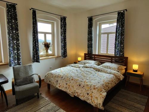 a bedroom with a bed and a chair and two windows at Velflík - ubytování v srdci Krušných hor in Abertamy