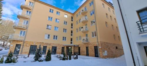 a large yellow building with snow in front of it at apartmán Argentum - Rezidence K Lanovce in Jáchymov