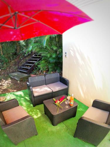 a patio with a couch and a red umbrella at Duplex Toti la - TropicalKaz Guadeloupe in Bouillante