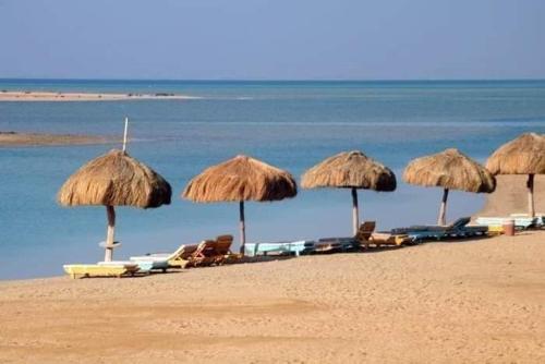 a group of straw umbrellas and chairs on a beach at Green Sudr Kitesurfing Hotel in Raʼs Matarma
