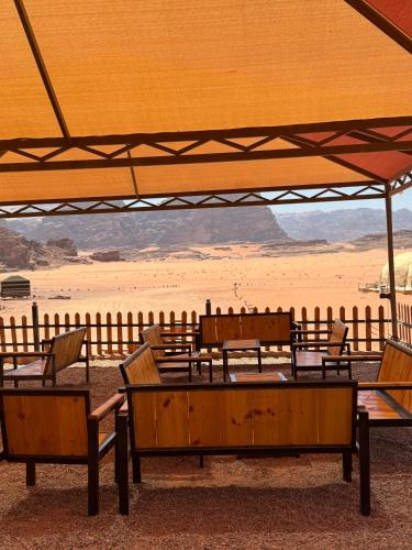 a group of wooden tables and chairs in front of a beach at Rum Angel Camp in Wadi Rum