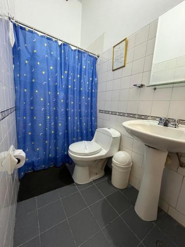a bathroom with a toilet and a sink and a blue shower curtain at El Cumbe Inn in Cajamarca