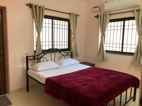 a bedroom with a bed with a red blanket and two windows at Mahalaxmi Homestay II in Mapusa