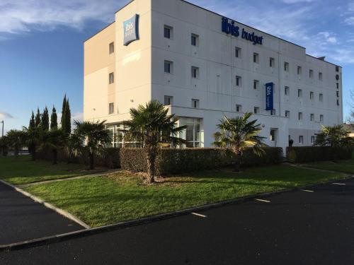 a white building with palm trees in front of it at Ibis Budget Ancenis in Mésanger