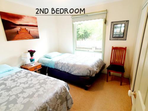 a bedroom with two beds and a window and a chair at Daylesford A Very Quiet ABELIA COTTAGE BOTANICAL COTTAGE 10 min walk town in Daylesford