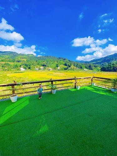 a boy standing on a green field with a fence at Moc's House bắc hà in Bắc Hà