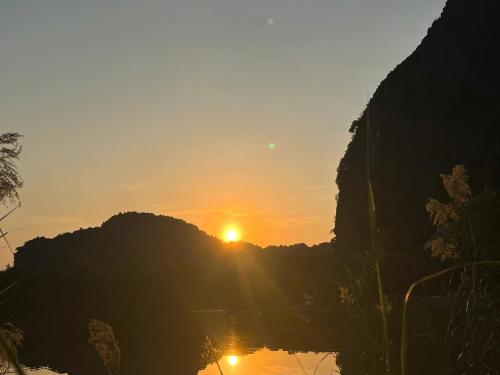 a sunset over a mountain with the sun in the sky at Tam Coc Golden Fields in Ninh Binh