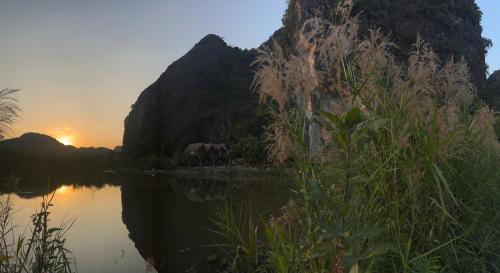 a body of water with the sun setting behind a mountain at Tam Coc Golden Fields in Ninh Binh