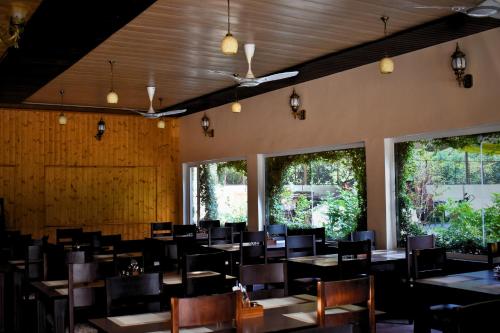 a dining room with tables and chairs and windows at The Greenwich resort in Rāmnagar