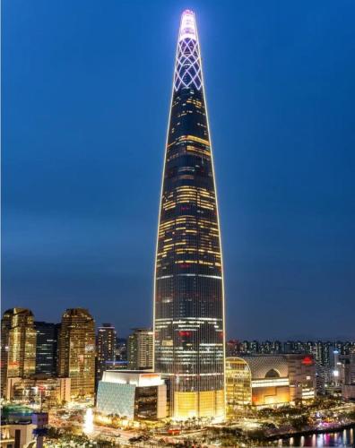 a tall building is lit up at night at 정스테이 서울 잠실 롯데월드 kspodome 아산병원 길동 코엑스 성수명동강남동대문 in Seoul