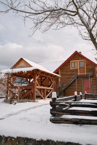 a log cabin in the snow with a house at Затишна Домівка in Slavske
