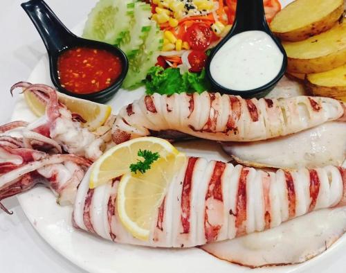 a white plate of seafood with lemon slices and dips at Moon house Beach Hostel in Haad Rin