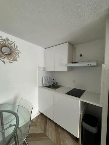 une cuisine avec des placards blancs et une table et une chaise en verre dans l'établissement Micro-maison 100m de la plage, au Barcarès