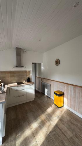 une cuisine avec des placards blancs et un tabouret jaune dans l'établissement Gîte La Grange de Pardies, à Orthevielle