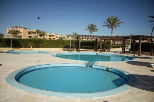 a group of three pools with palm trees and buildings at Green Sudr Kitesurfing Hotel in Raʼs Matarma