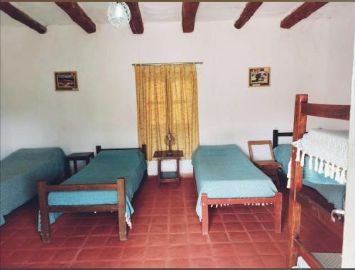a room with three beds and a table and a window at Alojamiento FINCA ENCANTO DEL VALLE in Cafayate