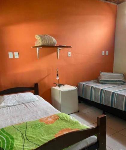 two beds in a room with orange walls at Pousada Roots in Itaúnas