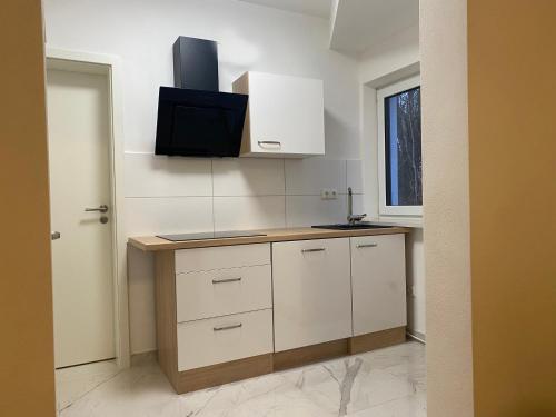 a kitchen with white cabinets and a tv on the wall at Apartments Y Edelhof in Saalfeld