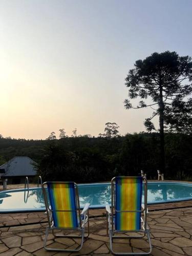 two chairs sitting in front of a swimming pool at Chácara da Aráucária - sítio privativo com piscina, churrasqueira e área verde in Presidente Lucena