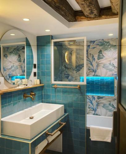 La salle de bains est pourvue de carrelage bleu, d'un lavabo et d'un miroir. dans l'établissement Hôtel Sèvres Saint Germain, à Paris