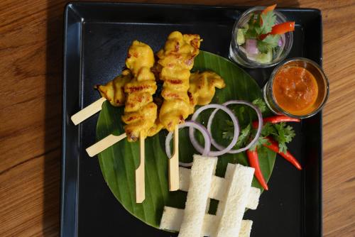 a plate of food with chicken skewers on a banana leaf at Cmor by Recall Hotels SHA Extra Plus in Chiang Mai